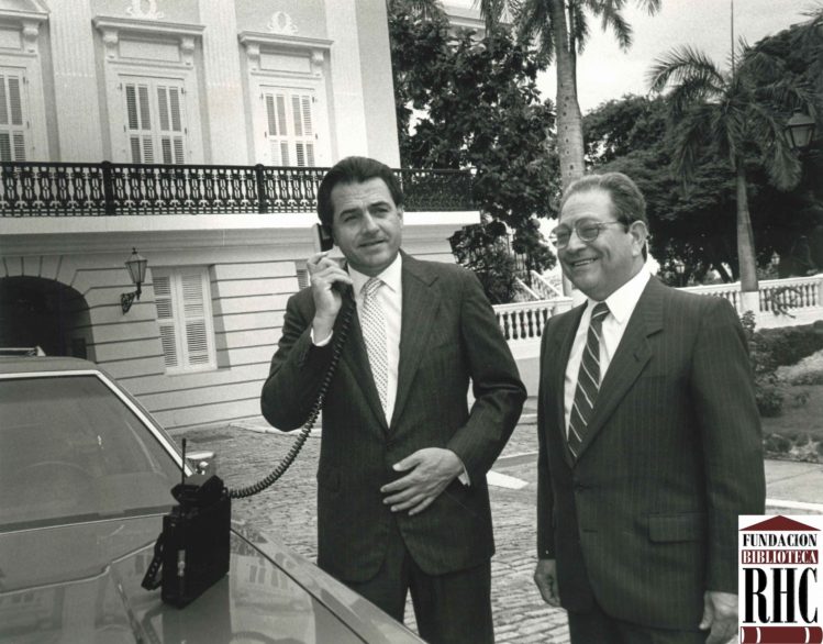 El Gobernador Rafael Hernández Colón y el presidente de la Puerto Rico Telephone Company, Pedro Galarza, posan frente a La Fortaleza mientras el primero realiza la llamada que inauguró el sistema de telefoní­a celular de la isla (foto: Fundación Biblioteca Rafael Hernández Colón)